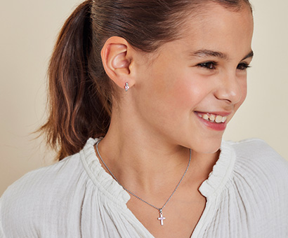 Mädchen trägt silbernen Schmuck mit Kreuzmotiv